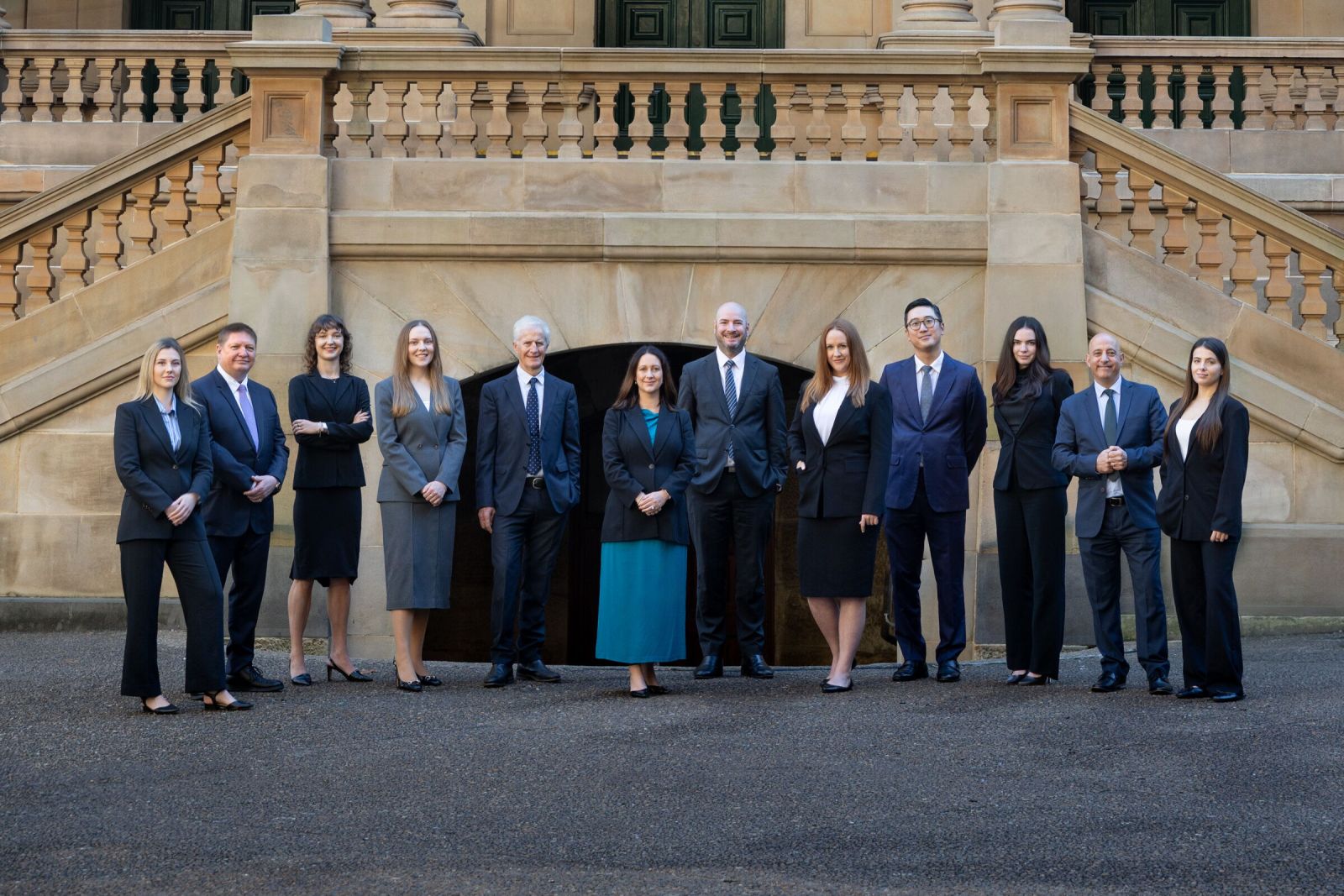 The Armstrong Legal team standing together in front of the sandstone staircase of a heritage courthouse building.